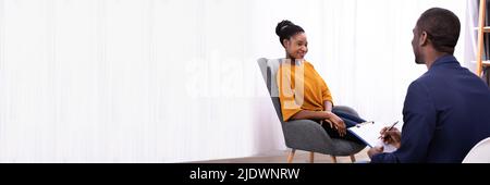 Young African Woman Sitting Near Psychologist With Clipboard To Treat Depression Stock Photo