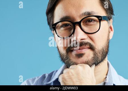 Asian bearded man in glasses standing against blue background Stock Photo