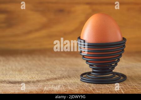 One boiled egg in a spiral-shaped metal support on wood background with copy space Stock Photo