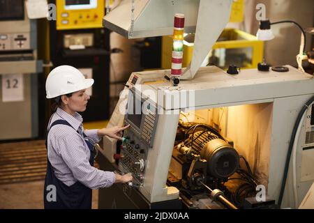 Serious busy female technical engineer standing at cnc lathe and pushing buttons while choosing Cnc machining operations at factory Stock Photo