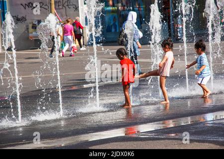 Vienna, Austria - 06.13.2022: Children frolic in the jets of the city fountain in the summer heat Stock Photo