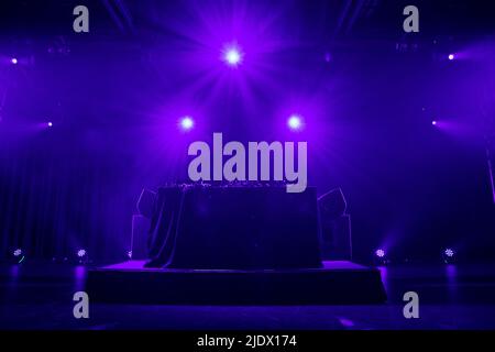 DJ booth set up on stage ready to be used with smoke and stage lighting Stock Photo