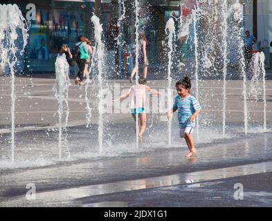 Vienna, Austria - 06.13.2022: Children frolic in the jets of the city fountain in the summer heat Stock Photo