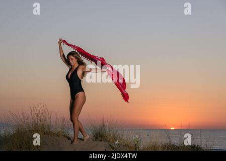 Happy, young woman in black swimsuit has fun on the seashore at sunrise Stock Photo