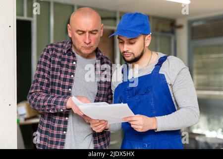 Customer discussing list of tasks with builder in house under renovation Stock Photo