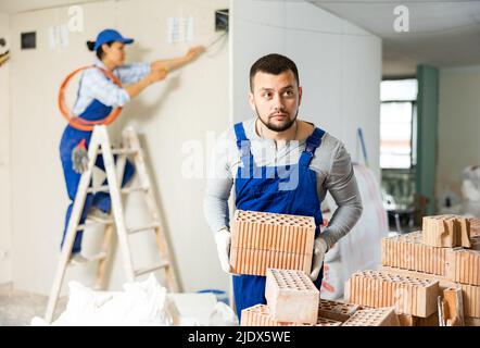 Man builder carrying bricks in construction site in apartment Stock Photo