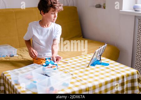 Kid collects robot from plastics details and programmed on tablet, robotics. Stock Photo
