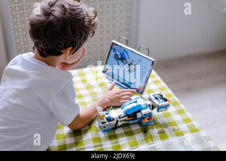 Kid collects robot from plastics details and programmed on tablet, robotics. Stock Photo