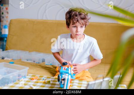 Kid collects robot from plastics details and programmed on tablet, robotics. Stock Photo