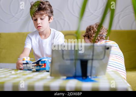 Kid collects robot from plastics details and programmed on tablet, robotics. Stock Photo