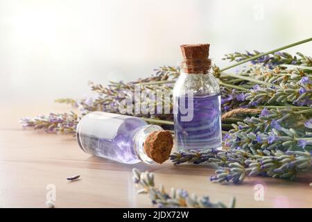 Two glass bottles with lavender extract on wooden table with bunch of spikes around.. Front view. Horizontal composition. Stock Photo
