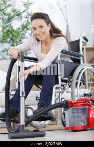 woman in wheelchair with vacuum cleaner Stock Photo