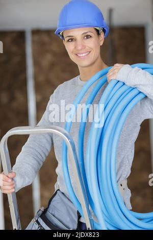 female builder on stepladder holding blue pipe Stock Photo