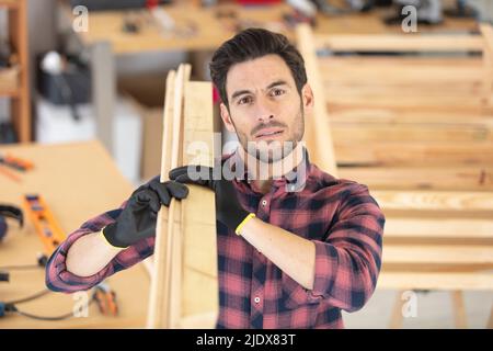 smiling mature carpenter carrying a wooden planks on his shoulder Stock Photo
