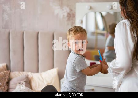Boy looking over shoulder holding toothbrush by mother at home Stock Photo
