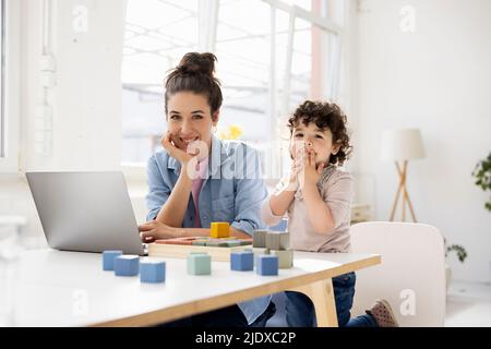 Mother working from home using laptop while daughter is playing with buiilding blocks Stock Photo