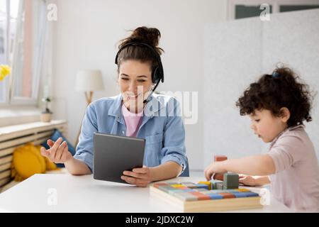 Mother working from home using digital tablet while daughter is playing with buiilding blocks Stock Photo