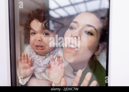 Mother and daughter looking through window pressing faces on glass pane Stock Photo