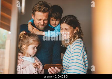 Happy man sharing smart phone with family seen through window Stock Photo