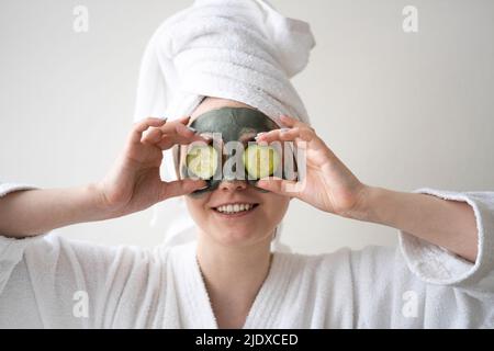 Happy woman holding slices of cucumber over eyes at home Stock Photo