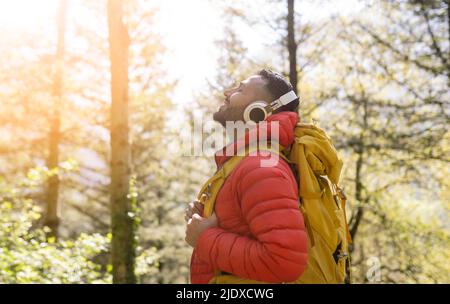 Smiling hiker wearing backpack enjoying music through wireless headphones in forest Stock Photo