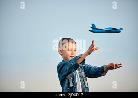 Boy playing with blue toy airplane in front of sky at sunset Stock Photo