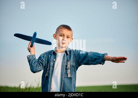 Cute boy playing with toy airplane in front of sky at sunset Stock Photo