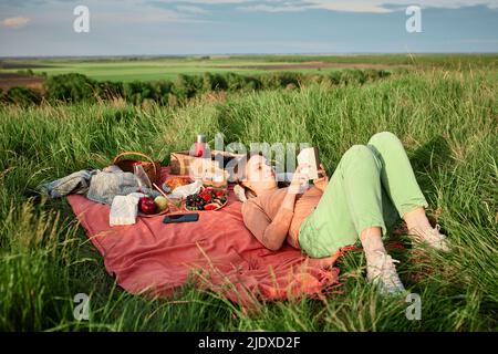 Smiling woman reading book at picnic in field Stock Photo