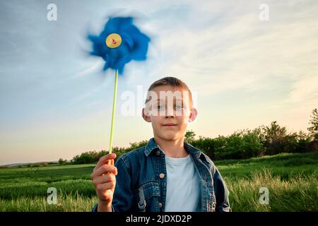 Cute boy holding blue pinwheel toy on field at sunset Stock Photo