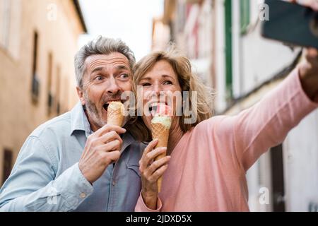 Happy tourists eating ice cream and taking selfie on smart phone Stock Photo