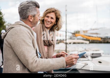 Smiling woman talking with man holding tablet PC at harbor Stock Photo