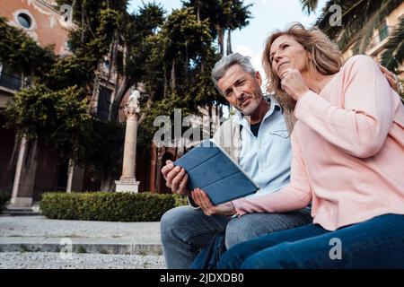Mature man using tablet PC by thoughtful woman in park Stock Photo