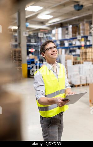 Smiling warehouse worker with tablet PC working in warehouse Stock Photo