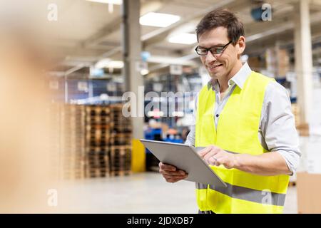 Smiling worker wearing eyeglasses using tablet PC in warehouse Stock Photo