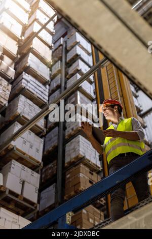 Smiling worker with tablet PC standing by railing in warehouse Stock Photo