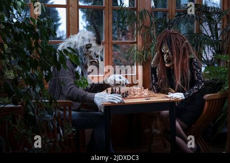 Man and woman in spooky costumes playing chess sitting at table Stock Photo