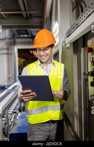 Smiling worker wearing hardhat using tablet PC in warehouse Stock Photo