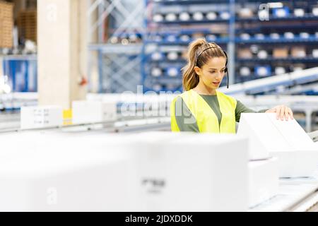 Worker wearing headset examining box in warehouse Stock Photo