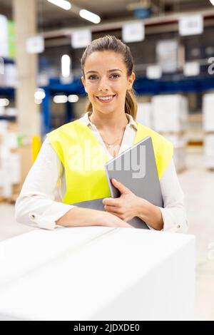 Smiling young worker with tablet PC standing by box in warehouse Stock Photo