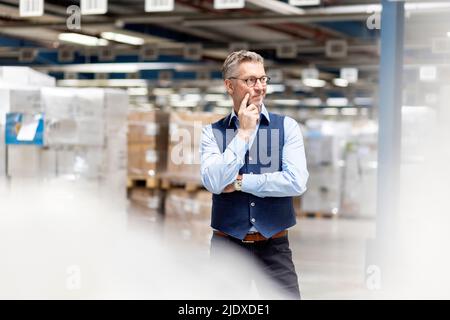 Thoughtful manager with hand on cheek standing in warehouse Stock Photo