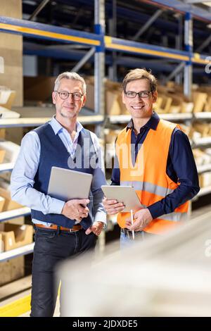 Smiling manager and worker with tablet PC standing in warehouse Stock Photo