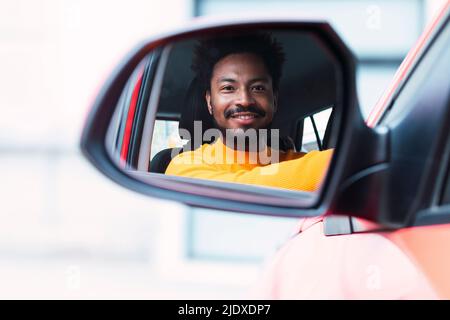 Smiling man looking through side-view mirror of car Stock Photo
