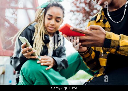 Young man using smart phone sitting by woman Stock Photo