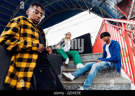 Young man standing by friends sitting on steps Stock Photo