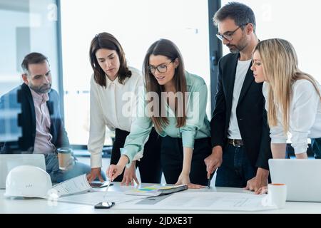 Businesswoman discussing plan over documents with colleagues at desk in office Stock Photo