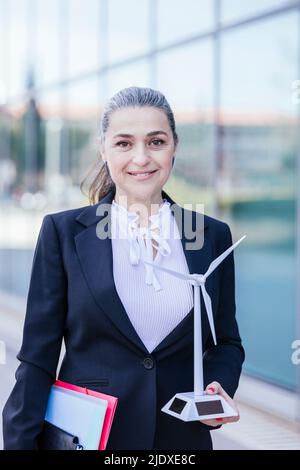 Mature businesswoman standing with document and wind turbine model Stock Photo