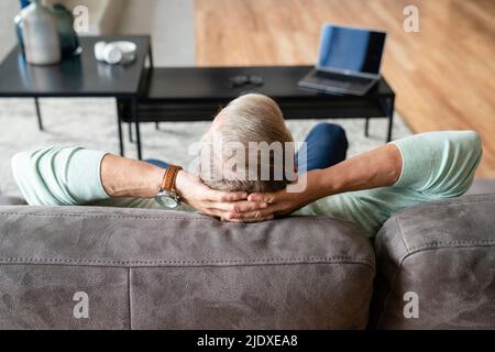 Man with hands behind head sitting on sofa at home Stock Photo