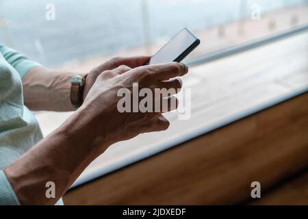Hands of man using smart phone by window at home