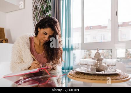 Mature woman writing in diary sitting at table Stock Photo