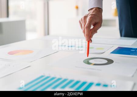 Hand of businessman with pen analyzing graphs and chart in office Stock Photo